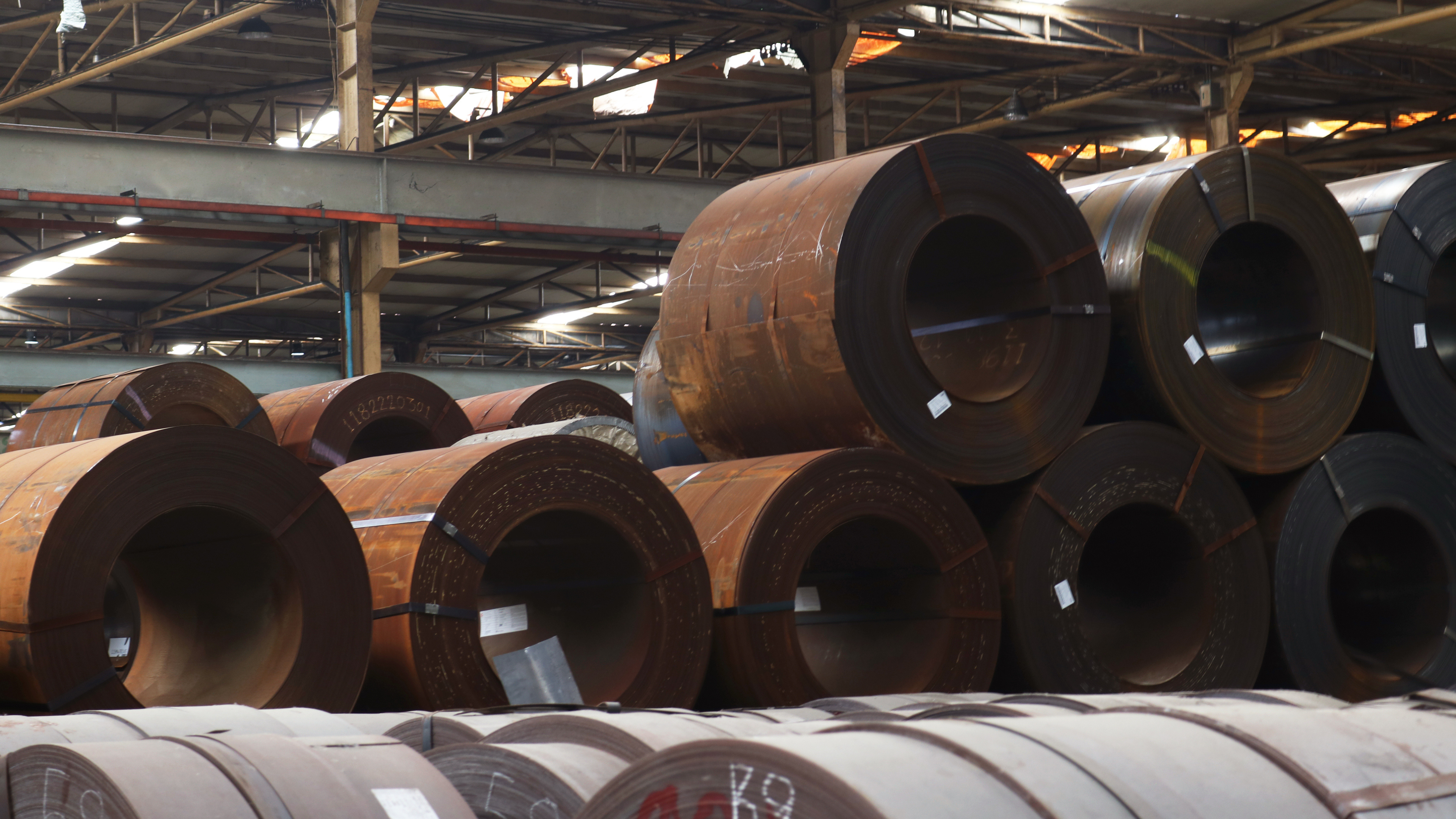 Large steel coils stacked in an industrial warehouse, ready for processing.